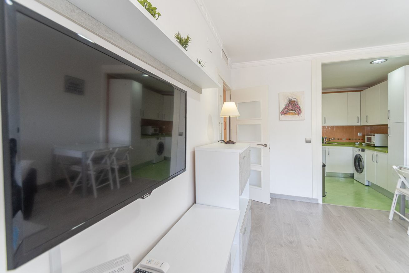 A modern living room with a large flat-screen TV, a sofa, a coffee table, and a dining area with chairs.