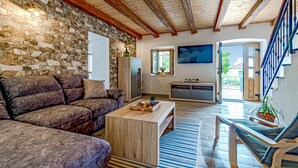 A living room with a stone wall, wooden ceiling beams, a sofa, a coffee table, a TV, and a staircase. - 2 bedroom amazing home in Orebic (Orebic)