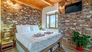 A bedroom with a stone wall, a bed with a geometric patterned bedspread, a bedside table with a lamp, and a potted plant. - 2 bedroom amazing home in Orebic (Orebic)