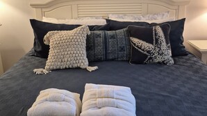 Un letto rifatto con cura, coperto da una trapunta blu scuro, con diversi cuscini e due asciugamani ripiegati.