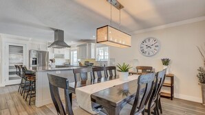 A modern kitchen with white cabinetry, a central island, and a dining area with a wooden table and chairs. - Staycation (Colorado Springs)