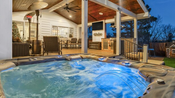 A hot tub with a wooden deck, a dining area with chairs, and a fireplace. - Staycation (Colorado Springs)