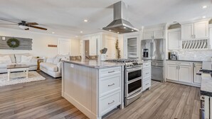 A modern kitchen with white cabinetry, a central island with a stove, and a built-in oven. - Staycation (Colorado Springs)