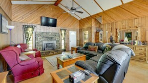 A spacious living room with a stone fireplace, leather sofas, and a television mounted on the wall. - Rural Arkansas Vacation Rental w/ Lake Access (Scranton)