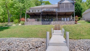 A two-story house with a stone foundation, a covered porch, and a wooden deck leading to the entrance. - Waterfront Smith Mountain Lake Home w/ Boat Dock! (Goodview)