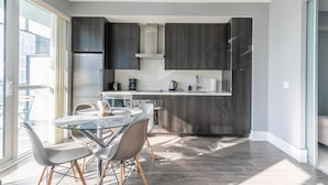 A modern kitchen with dark wood cabinets, a glass dining table, and a view of the city through large windows. - GLOBALSTAY.  Design 26Floor Downtown Apartment (Toronto/Canada)