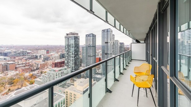 A balcony with a city view, a yellow chair, and a glass railing. - GLOBALSTAY. Executive 2BR 2BA Condo in DT. Gym, Pool, Hot Tub (Toronto/Canada)