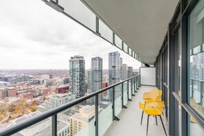 A balcony with a city view, a yellow chair, and a glass railing.