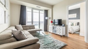 A modern living room with a sofa, a glass coffee table, a TV on a white cabinet, and a view of the city through large windows. - GLOBALSTAY. Executive 2BR 2BA Condo in DT. Gym, Pool, Hot Tub (Toronto/Canada)