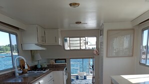 Une cuisine compacte avec un plancher en bois, des armoires blanches et une vue sur l’eau par une fenêtre.