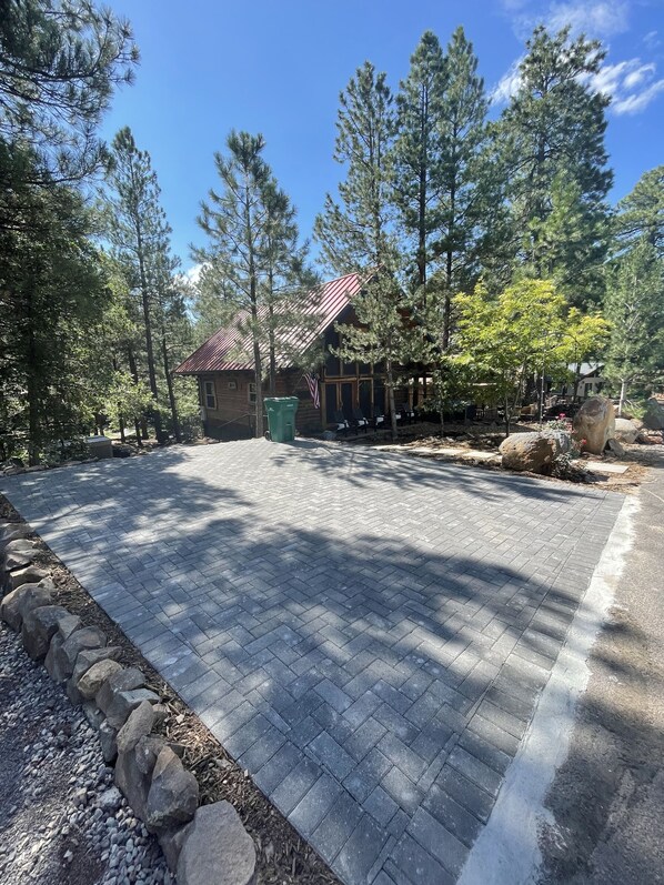 Un chalet doté d’une allée pavée, entouré de grands pins et bordé d’un petit bâtiment à toit rouge.