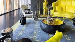 Uma sala de estar moderna com uma janela grande, um sofá amarelo, uma mesa de centro preta e um espelho decorativo.