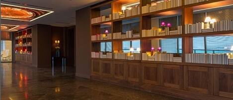 A spacious lobby with a large wooden bookshelf, a decorative ceiling, and a polished floor.