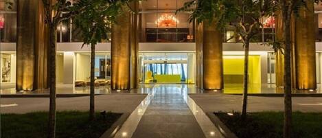 A modern building with a central entrance, large pillars, and a reflective pathway leading to the entrance.