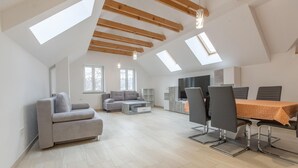 Un appartement-loft spacieux avec de hauts plafonds, des fenêtres de toit, un coin repas avec une table et des chaises, un canapé et un téléviseur.