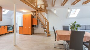 Un vaste loft doté d’un escalier en bois, d’un coin repas et d’une cuisine avec des meubles de couleur orange.