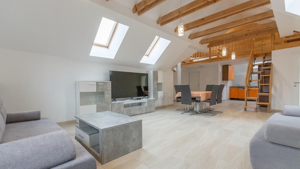Un salon moderne doté d’un téléviseur à écran plat, de canapés gris, d’une table basse et d’un coin repas avec une table et des chaises.