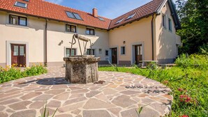 Un bâtiment doté d’une cour en pierre, d’un puits et d’un toit recouvert de tuiles rouges.