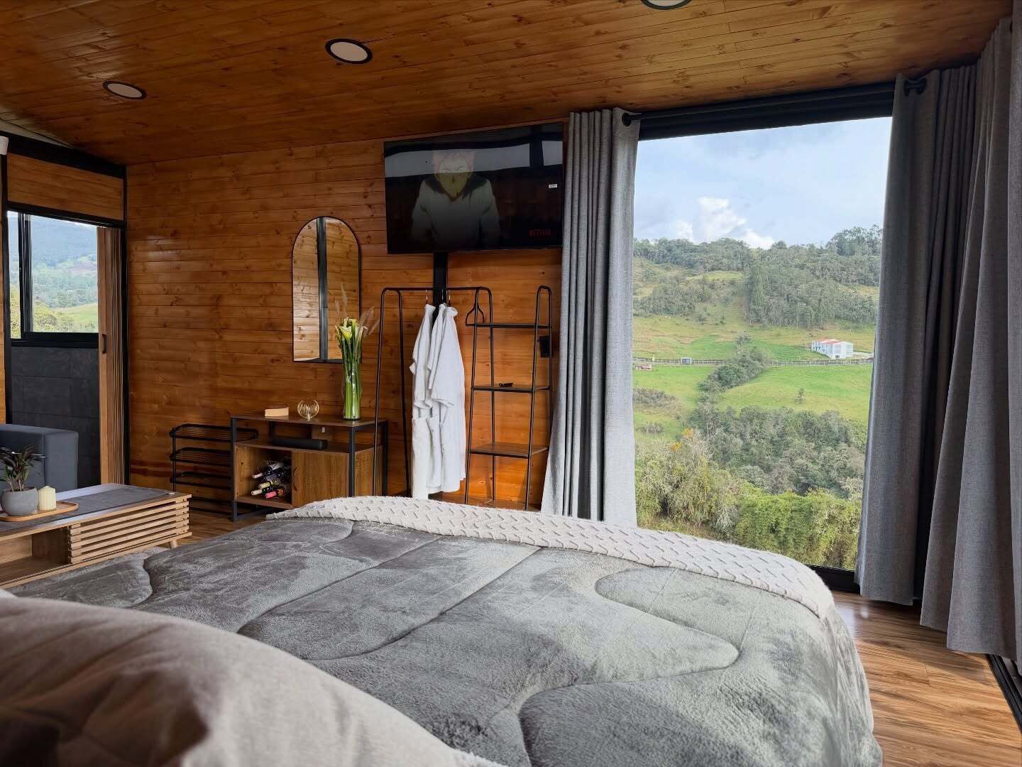 Une chambre avec un grand lit, un plafond en bois, une télévision, un miroir, un bureau et une vue sur la campagne.