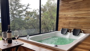 A wooden deck with a hot tub, two wine glasses, and a bottle of wine.
