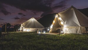 A campsite with multiple tents illuminated at dusk, surrounded by grass and mountains. - Andean Glamping (Pisac)