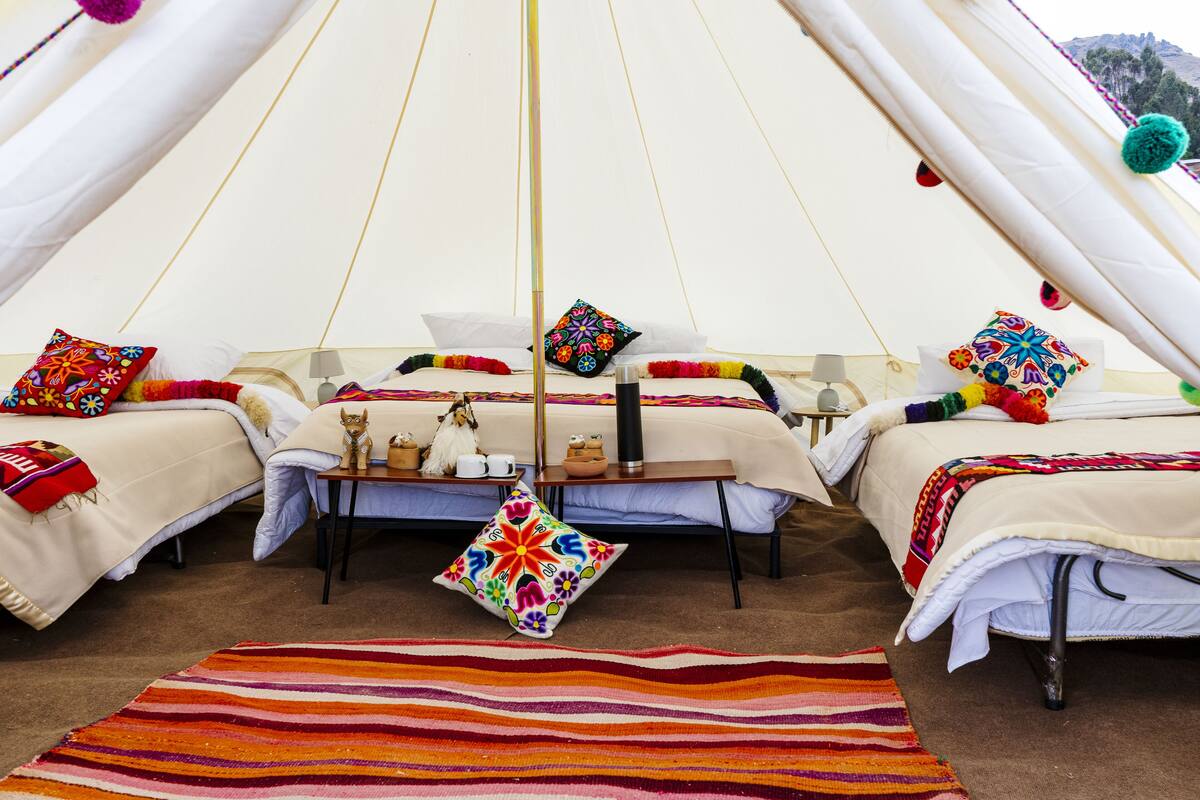 A cozy interior of a tent with two beds, colorful pillows, a small table, and a striped rug.