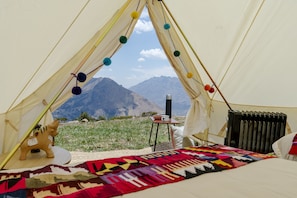 Una carpa con una cama, una manta, una mesita con un hervidor y vistas a montañas.