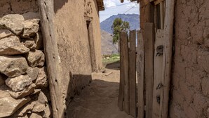 A narrow alleyway with a stone wall on one side and wooden doors on the other, leading to a mountainous landscape. - Andean Glamping (Pisac)
