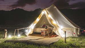 A tent with a bed inside, surrounded by a grassy area and a mountain in the background. - Andean Glamping (Pisac)