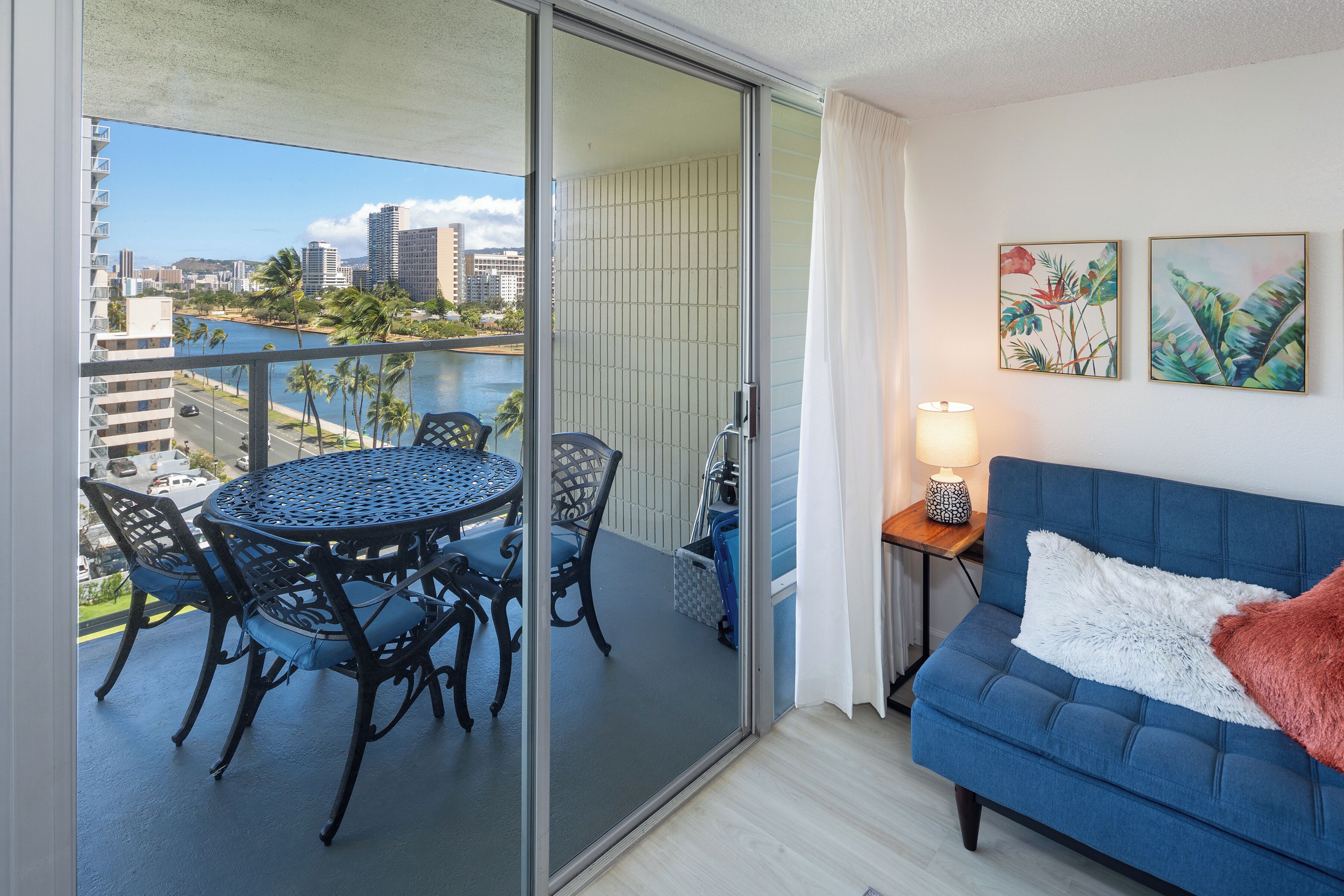 A balcony with a table and chairs, a sofa, and two framed pictures on the wall.