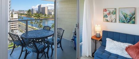 A balcony with a table and chairs, a sofa, and two framed pictures on the wall.