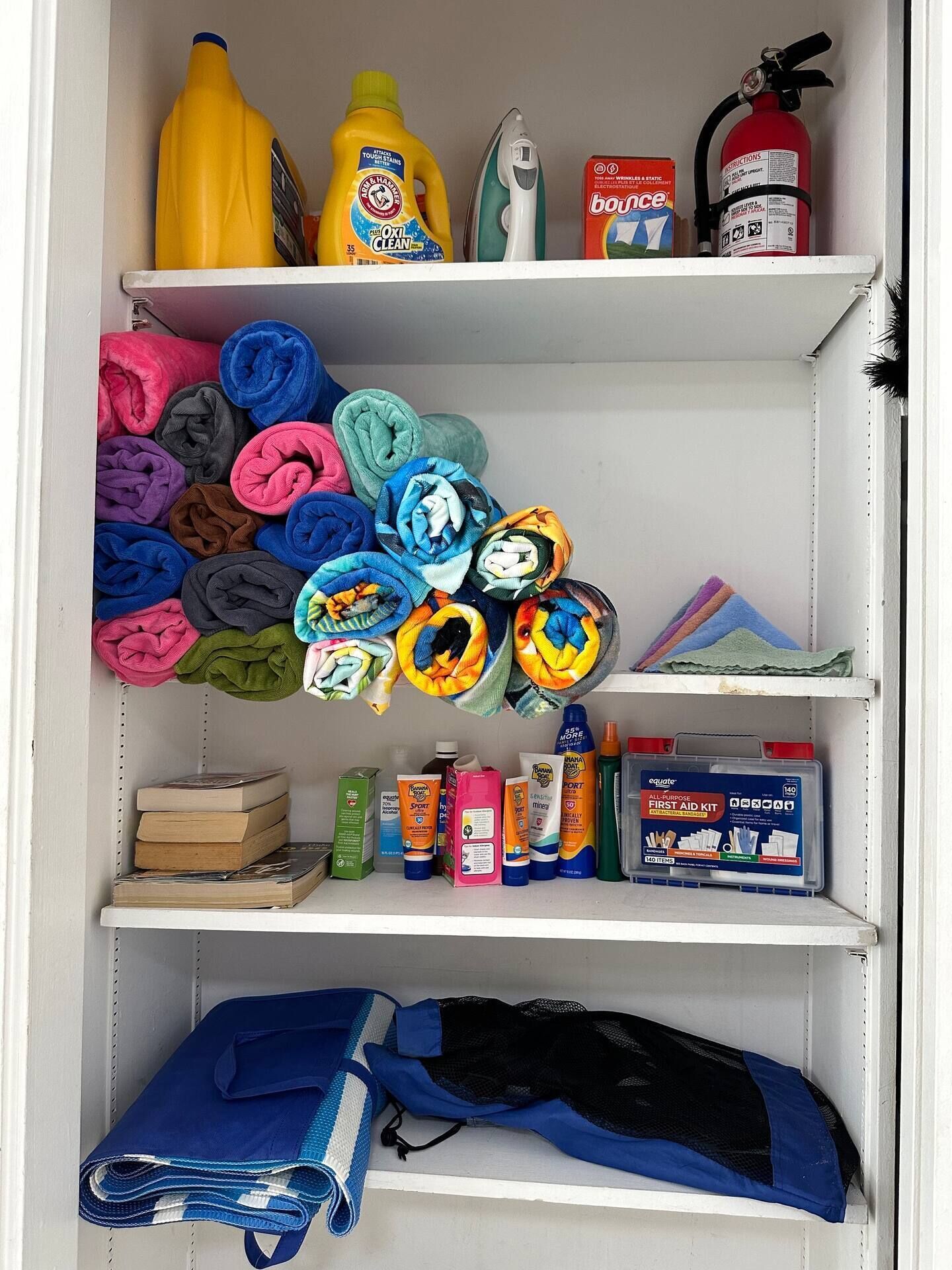Une étagère de rangement contenant des serviettes pliées, des produits de nettoyage, un extincteur et une trousse de premiers secours.