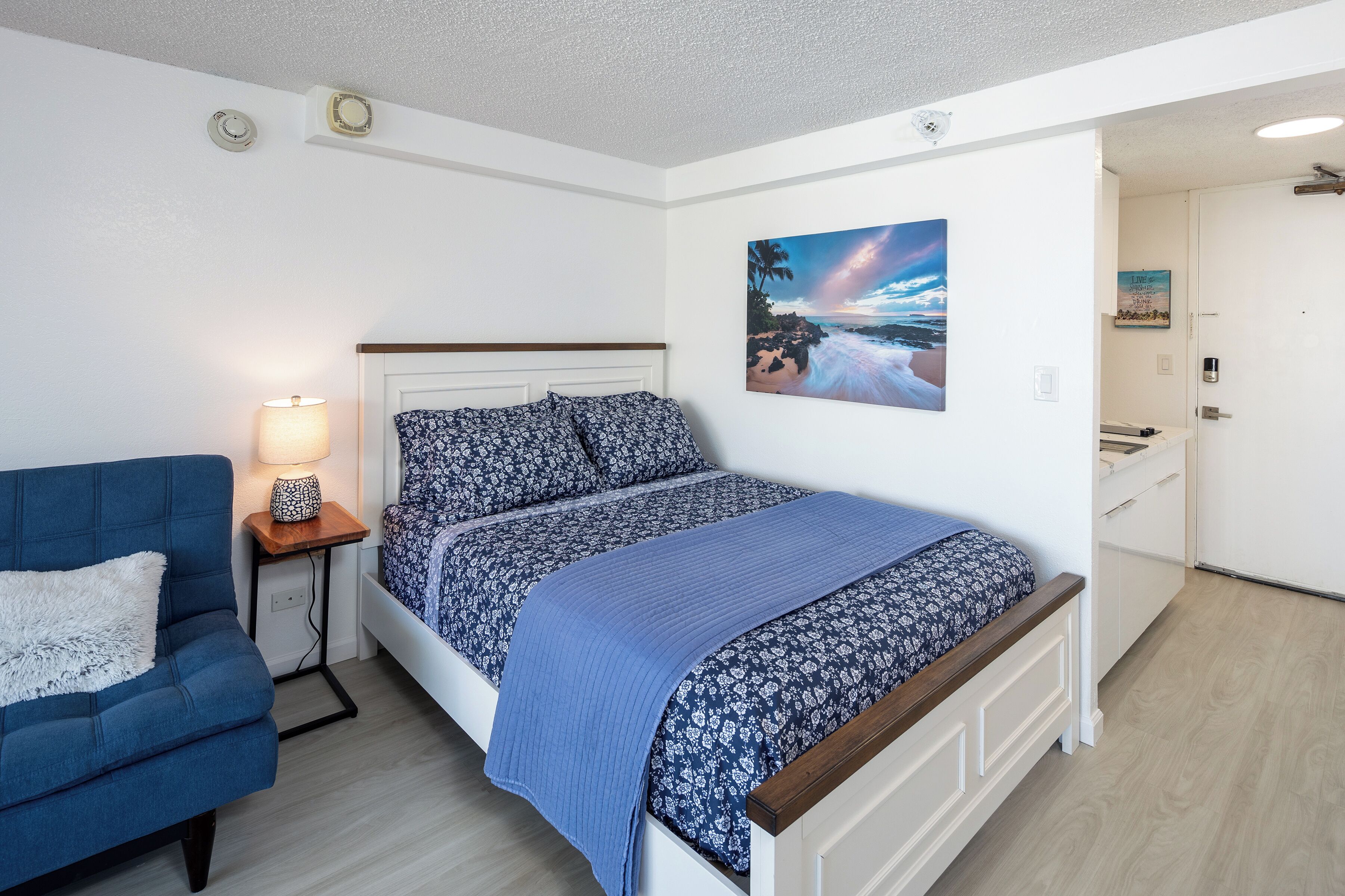 Una camera da letto con un letto, un divano blu, un comodino con una lampada e un quadro appeso al muro.