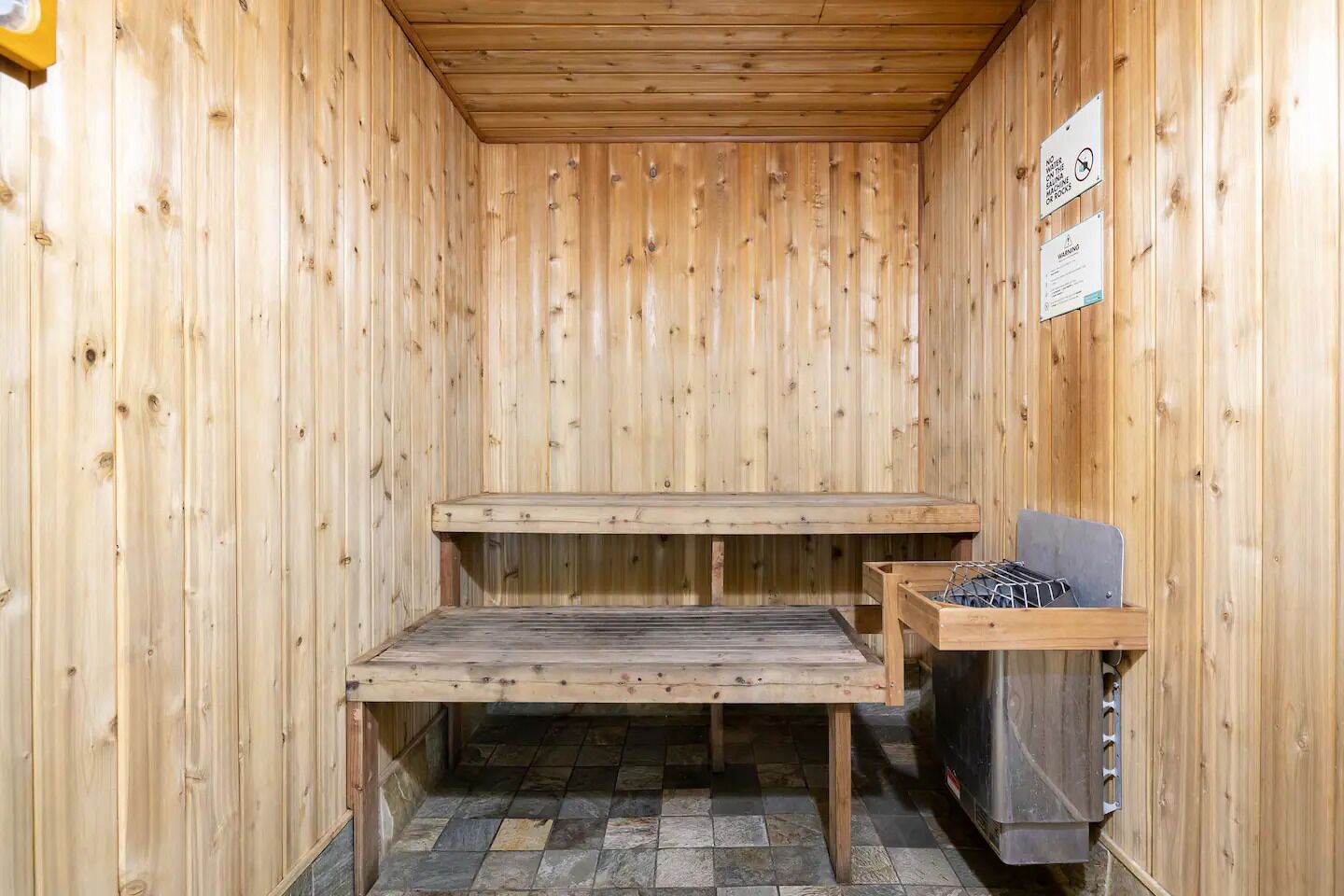 A sauna with two benches and a metal rack, wooden walls, and a tiled floor.