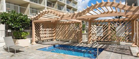 Ein Poolbereich mit einer Holzpergola, Liegestühlen und einem Pool mit blauer Fliesenbordüre.