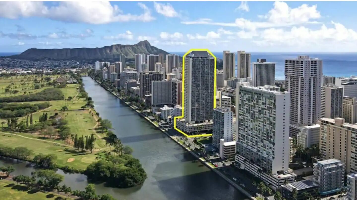 Un edificio alto dal design architettonico moderno, circondato da un fiume e da vegetazione.