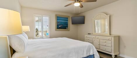 A bedroom with a bed, a ceiling fan, a TV, a dresser, and a window with blinds.