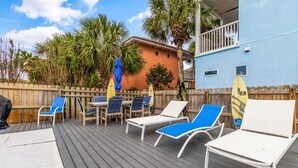 A wooden deck with lounge chairs and a table, surrounded by a wooden fence and palm trees. - Here Comes Sunshine by Southern Vacation Rentals (Miramar Beach)