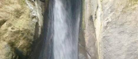 A person standing in a natural water pool with a waterfall behind them.
