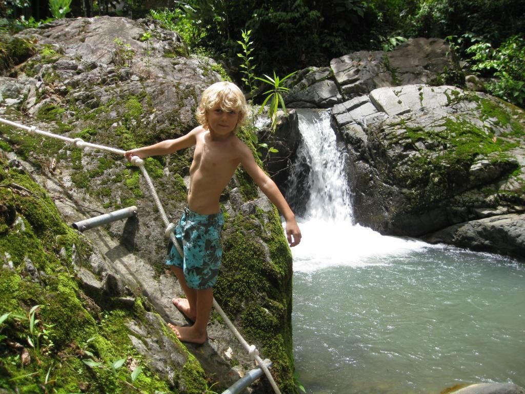 Iemand staat op een met mos begroeide rots bij een waterval.
