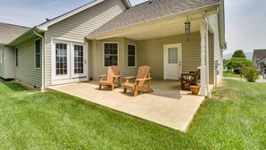 Een gelijkvloers huis met een overdekte patio, compleet met twee Adirondack-stoelen en een tafel.
