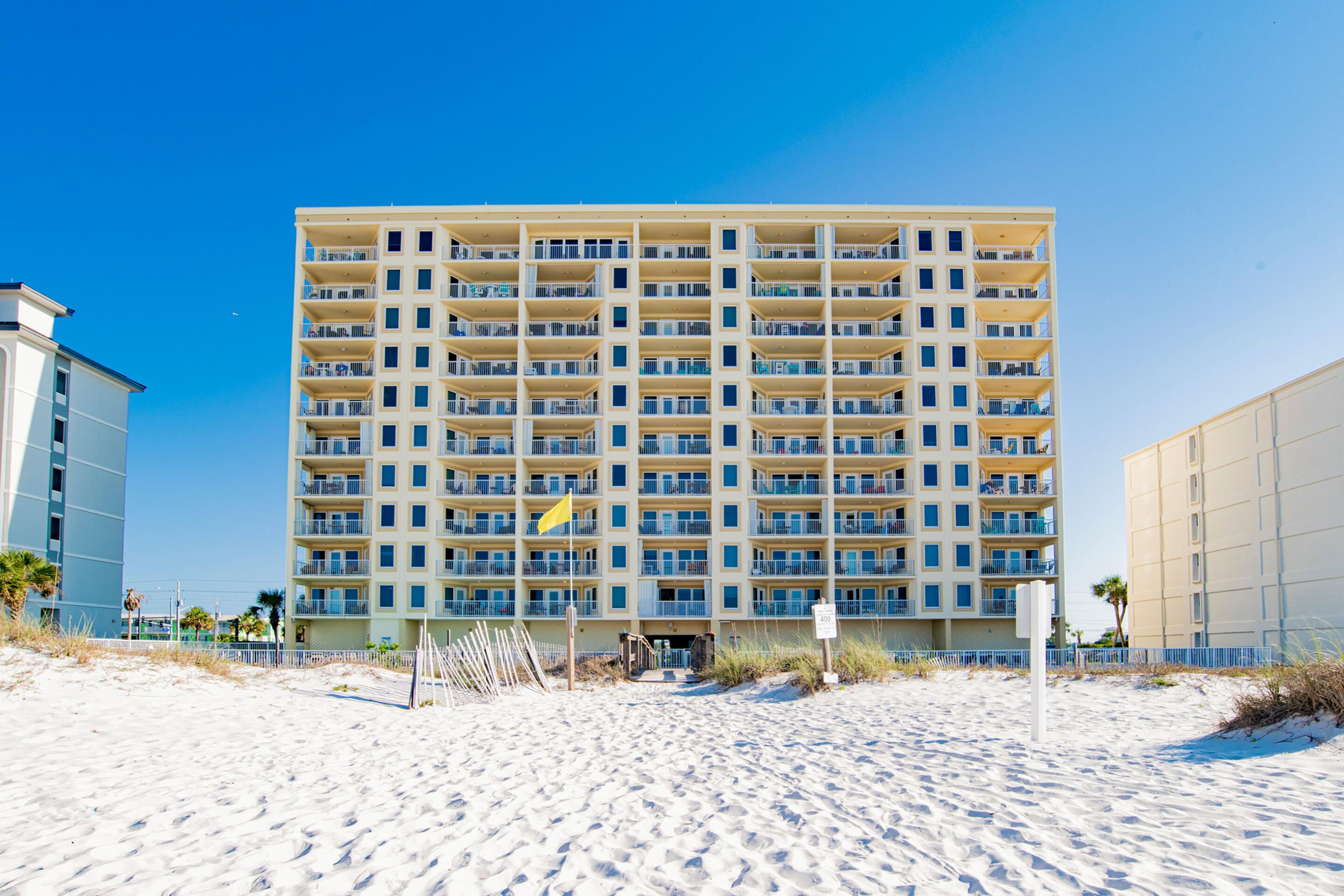 Ein mehrstöckiges Hotel mit Balkonen, direkt an einem Sandstrand gelegen.