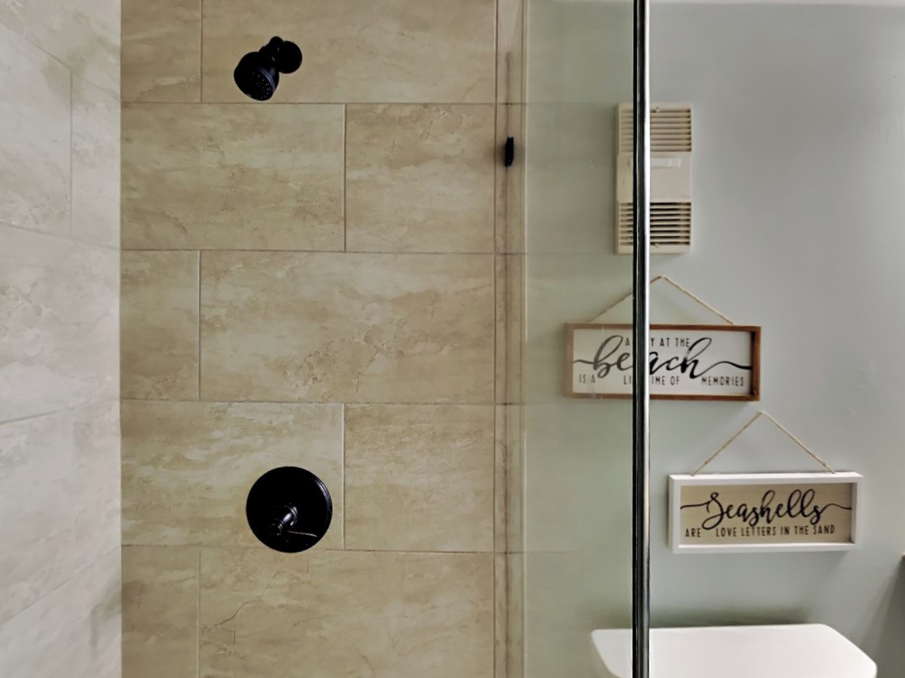 Een moderne badkamer met een douchecabine van glas, beige tegels, een toilet en twee decoratieve borden aan de muur.