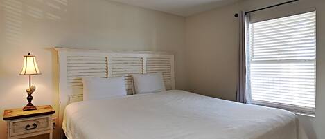 A bedroom with a bed, a nightstand with a lamp, and a window with blinds.