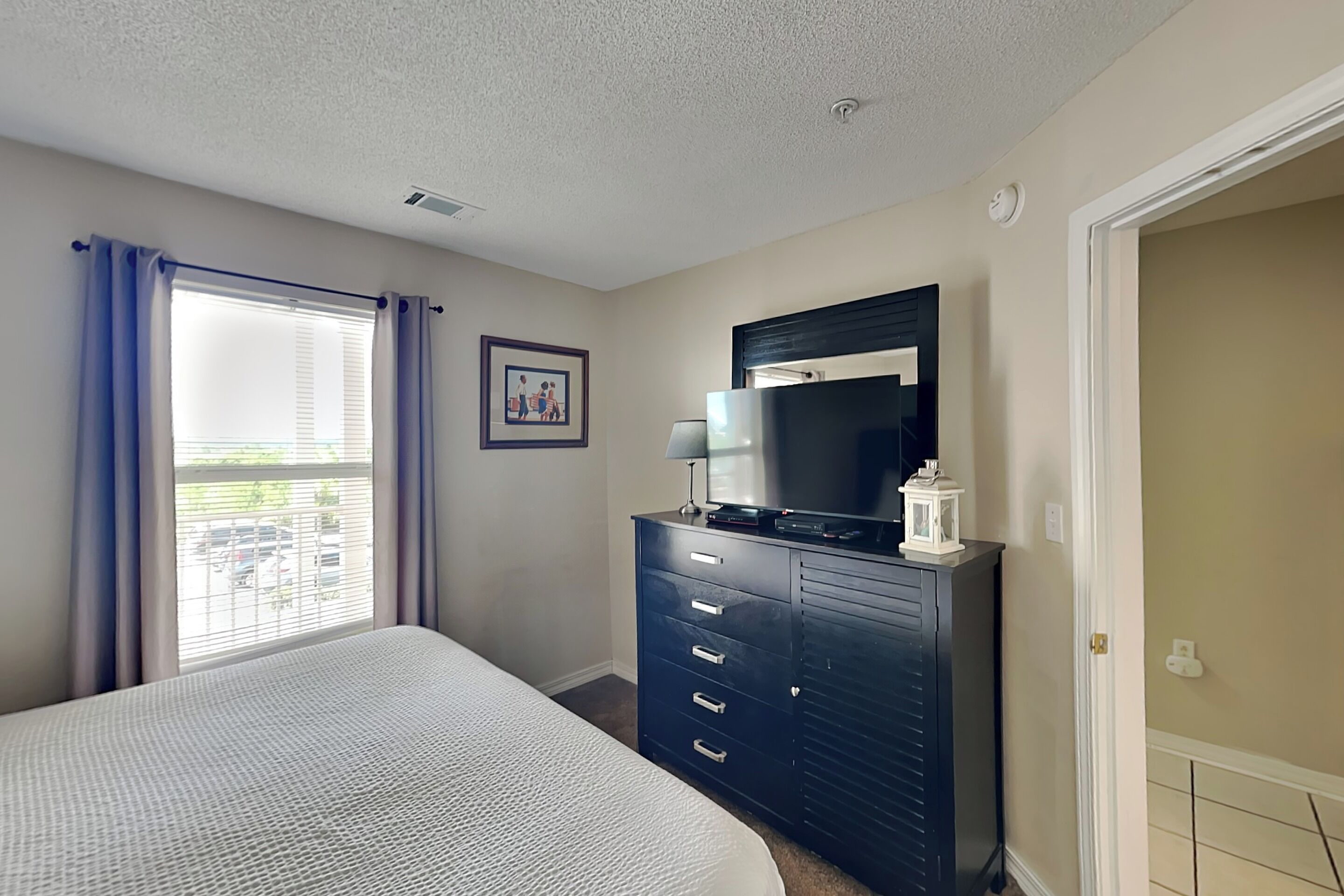 A bedroom with a bed, a dresser, a television, and a window with curtains.