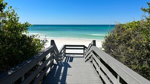 A wooden boardwalk leading to a beach with clear blue water and a sandy shore.