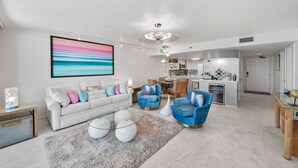 A modern living room with a white sofa, blue armchairs, and a large abstract painting.
