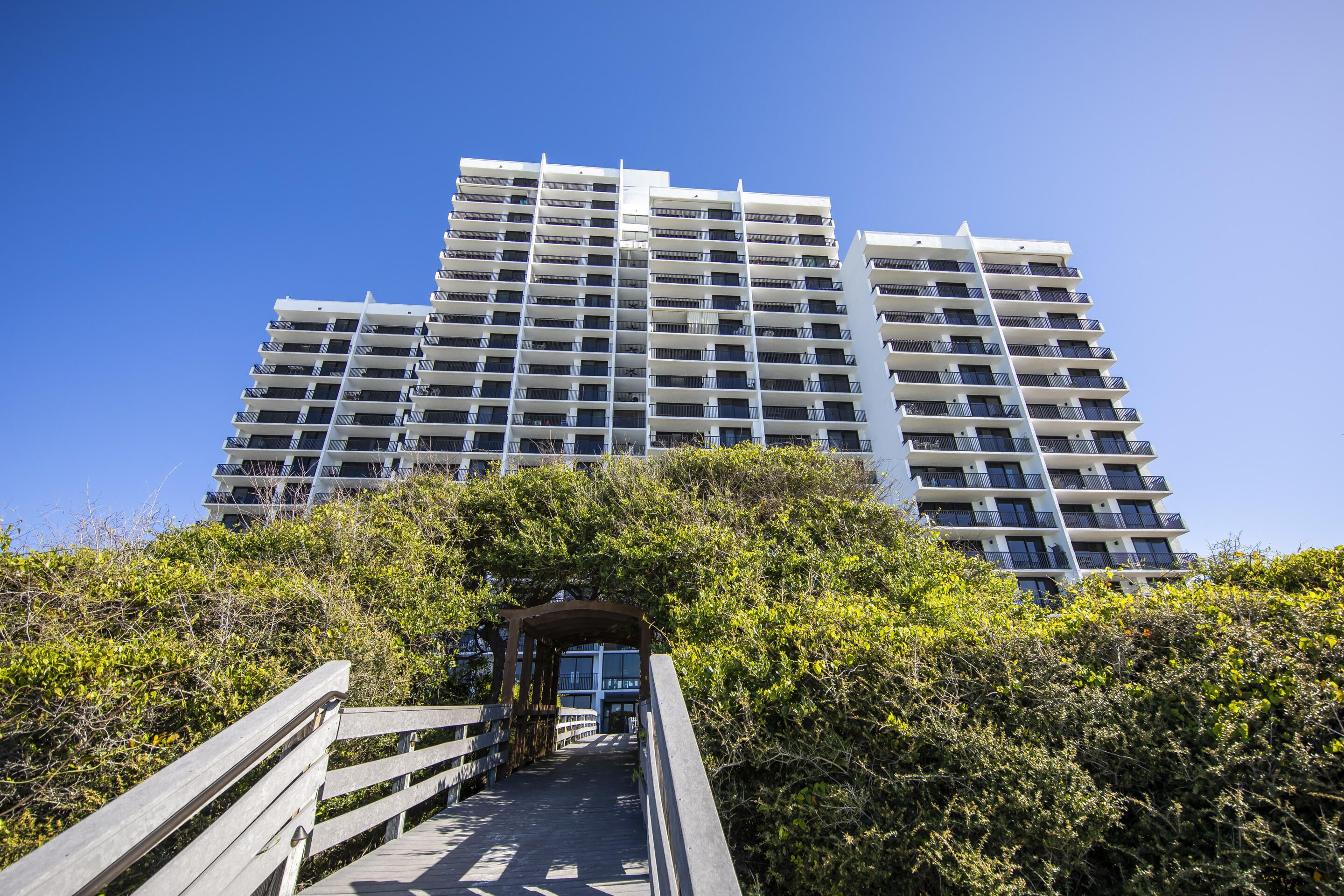 A multi-story building with a central staircase leading to an entrance, surrounded by dense greenery.