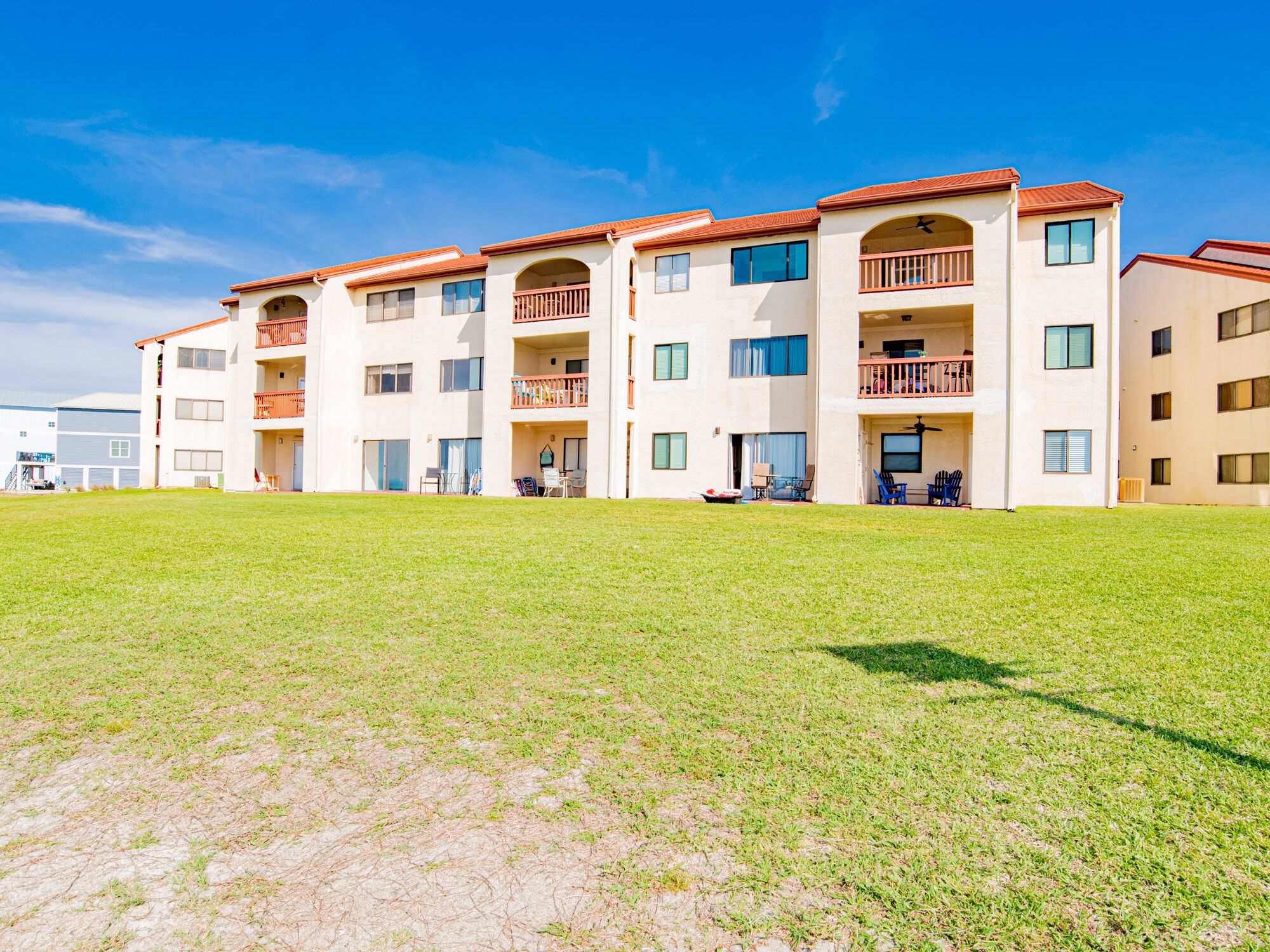 A multi-story residential building with balconies, a flat roof, and a grassy courtyard.