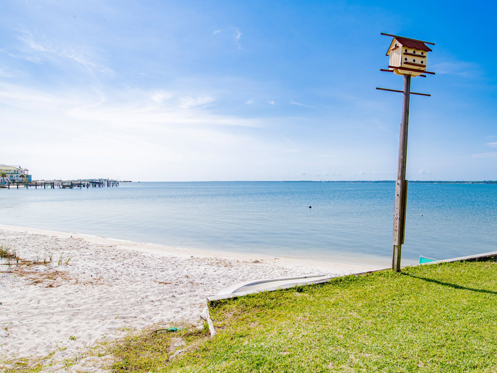 A beach with a wooden birdhouse on a pole, a pier in the background, and a clear sky.